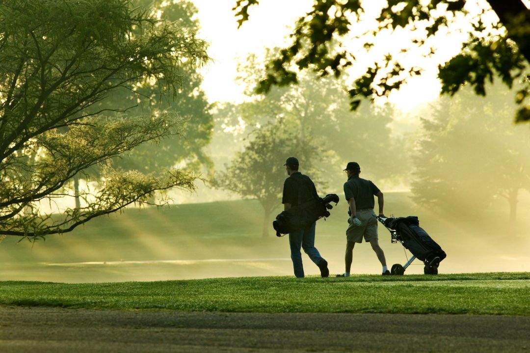 River Road Estates resident golfers walking on a golf course with the sun streaking through the trees on a beautiful summer morning